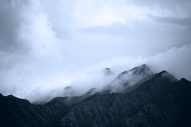 Mavi renkli dramatik dağ zirveleri sis, sis ve dramatik bulutlu gökyüzü ile örtülmüş. Alçak ufuk metin için mükemmel ya da uzay reklamını kopyala.