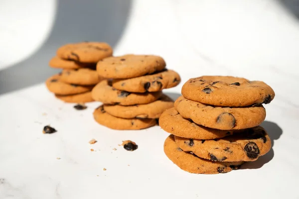 Stacks of chocolate chip cookies with pieces of chocolate in sun light with shadows. Recipe of oatmeal biscuits with chocolate chips. Homemade bakery.