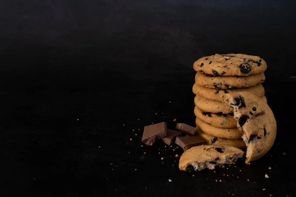 Stack of chocolate chip cookies on black background with copy space. Recipe of tasty biscuits with pieces of chocolate. Dessert menu for restaurant or cafe. Delicious cookies with chocolate crumbs.