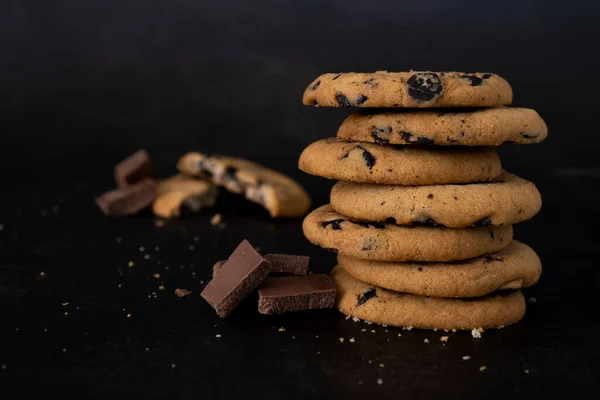 Stack of chocolate chip cookies on black background. Recipe of tasty biscuits with pieces of chocolate. Dessert presentation for restaurant or coffee house. Delicious cookies with chocolate crumbs.