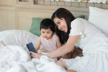 Güzel bebek, annenle bir fotoğraf çek ve yatakta otur.