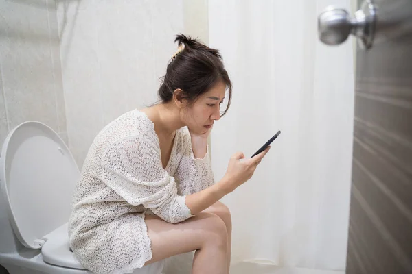 asian woman on toilet with cell phone. Woman sitting with mobile in toilet