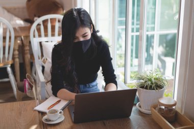 Maske takan ve laptopla çalışan genç kadınlar kafenin ahşap masasında, iş konsepti