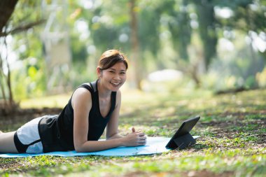 Genç bir kadın parkta bir video konferansında yoga egzersizi öğreniyor. Spor yoga konsepti.