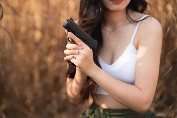 Beautiful asian women aim the gun on dry grass background