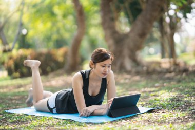 Genç bir kadın parkta bir video konferansında yoga egzersizi öğreniyor. Spor yoga konsepti.