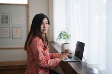 Kafenin pencere eşiğinde çalışan dizüstü bilgisayar kullanan kadın grafik tasarımcısı