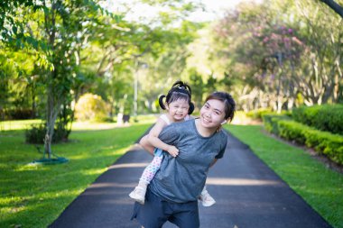Şirin kız, annesiyle birlikte bahçede sırtına binmiş.