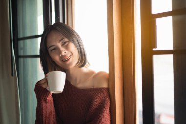 Güzel kadınlar yatak odasındaki pencerenin yanında sıcak kahve içiyorlar.