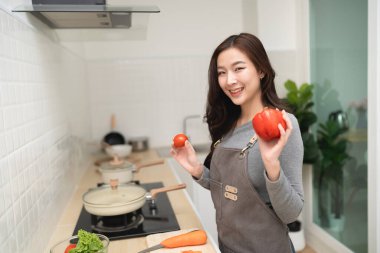 Mutfakta elinde olgun kırmızı domateslerle neşeli genç bir kadın sağlıklı bir yemek hazırlarken, canlı malzemeler ve aşçılık becerileri sergiliyor.