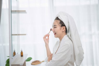 Kadın, Yeşil Bitkiler ve Doğal Işıklar ile Parlak Modern Banyo 'da Saç Sarılı Havlularla Evde Cilt Rutini Uygulıyor