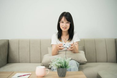 Evde video oyunu oynayan genç bir kadın, elinde bir kontrolörle boş zamanların tadını çıkaran şık dekorları ve bitkileri olan rahat bir oturma odası atmosferi olan bir kadın.