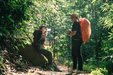 Bir tanesi su içerken diğeri de canlı doğa ile çevrili bir baston tutarken, maceraperest yürüyüşçüler yemyeşil ormanda mola veriyorlar.