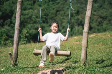 Çevrelerinde bereketli doğa ve parlak güneş ışığıyla çevrili Yeşil bir tarlada salıncağın keyfini çıkaran Çocuk Güzel bir günde neşeli bir ifadeyle