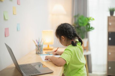 Ev masasındaki kağıt üzerine sanatsal çizimler yapan küçük bir çocuk rahat, parlak bir ortam, ev bitkileri ve renkli yapışkan notlarla süslenmiş.