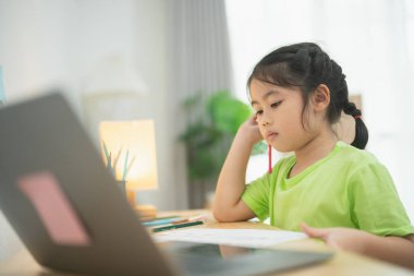 Ev ödevine laptopuyla, renkli kırtasiyeyle ve rahat bir çalışma alanıyla odaklanan genç kız evde çevrimiçi öğrenim görüyor.