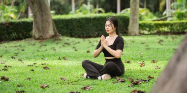 Yeşil çimenler üzerinde farkındalık meditasyonu yapan bir kadının sakin bir sahnesi, ağaçlar ve düşen yapraklarla çevrili, rahatlama ve iç huzuru somutlaştıran.