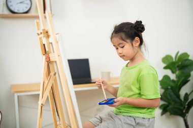 Parlak ve modern bir odada tuvalde resim yapan genç kız, öğrenme ve hayal gücüne odaklanmış yaratıcılık ve sanatsal ifade sergiliyor.