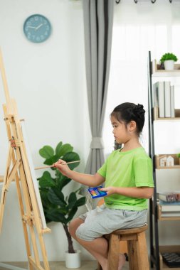 Genç ressam, modern parlak odada tuvale renkli sanat eserleri çizmeye odaklanmış, sanat yoluyla yaratıcılık ve hayal gücünü sergiliyor