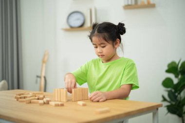 Parlak bir odada tahta bloklarla oynayan, yaratıcı oyun zamanı etkinliğine katılan, inşa ve öğrenme becerilerine odaklanan çocuk.