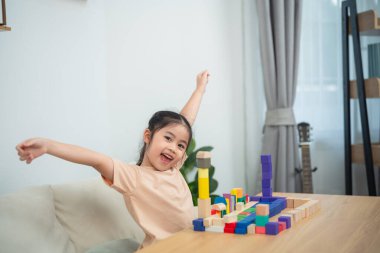 Parlak oturma odasında renkli yapı taşlarıyla oynayan mutlu genç kız kameraya gülümserken yaratıcı aktivitelerden zevk alıyor.