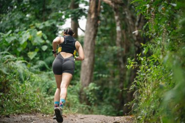 Dişi koşucu yemyeşil orman yolunda koşuyor, doğanın tadını çıkarıyor, spor yapıyor, sağlıklı yaşam tarzı, atletik hareketi, açık hava egzersizi, huzurlu bir ortam.