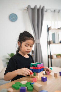 Genç kız renkli ahşap bloklarla yaratıcı bir oyun oynuyor. Parlak ve neşeli bir oturma odasına bir kule inşa etmeye odaklanmış.