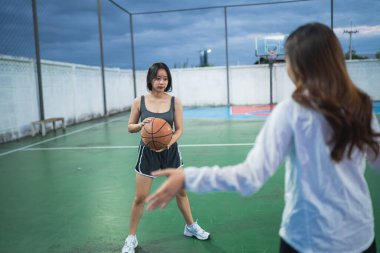 Odaklanmış İfadeler ve Atletik Giyimlerle Dramatik Bulutlu Gökyüzü Altındaki Mahkeme 'de Açık Basketbol Çalışması Yapan İki Genç Kadın