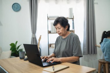 Modern ev ofis ortamında dizüstü bilgisayar kullanan üst düzey bir kadın, ahşap masada otururken ekrana odaklanmış, çalışma alanını aydınlatan doğal ışık
