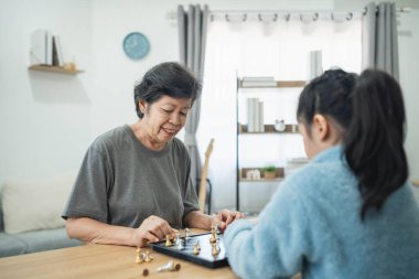 Samimi bir oturma odasında satranç oynarken, büyükanne ve torunu arasında geçen bir an. Ilık Doğal Işıkla ayarlanıyor.