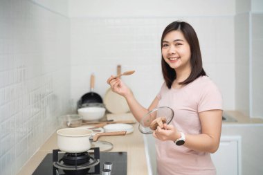 Modern Mutfakta Mutlu Genç Kadın Aşçılığı, Kaşık ve Lid Tutarken Gülümseme, Neşeli Atmosferle Sağlıklı Yemek Hazırlama