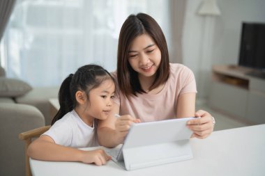 Genç anne ve kız evlerinde tablet kullanarak öğrenim faaliyetlerine girişiyor. Parlak ve rahat bir oturma odasında, teknoloji ve bağlantı sergiliyor.