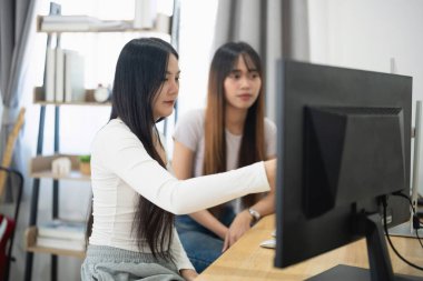 İki genç kadın, dijital proje tartışması ve takım çalışması stratejisine odaklanarak, parlak ve modern bir çalışma alanında bir bilgisayarda işbirliği yapıyorlar.