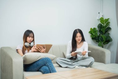 Kanepede keyif çatan, rahat bir oturma odasında kitap okuyup rahatlayan iki genç kadın.