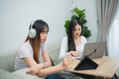 Doğal Işıklı Konforlu Bir Oturma Odasında Dijital Faaliyetler Yapan İki Kadın, Biri Kulaklık Giyen ve Biri Küçük Bir Masada Dizüstü Bilgisayar Kullanan Kadın