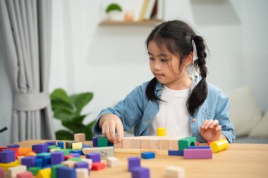 Evdeki masada renkli ahşap yapı taşlarıyla oynayan sevimli Asyalı kız. Yaratıcı oyuncaklar sayesinde mutlu çocuk öğreniyor ve hayal gücünü geliştiriyor.