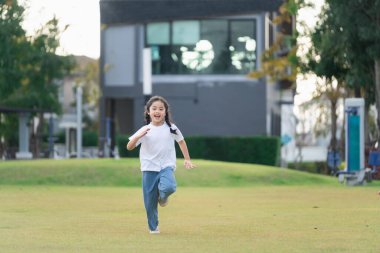Gündüz vakti yeşil bir parkta özgürce koşan neşeli genç kız, açık havada mutluluk ve enerji gösterisi yapıyor.