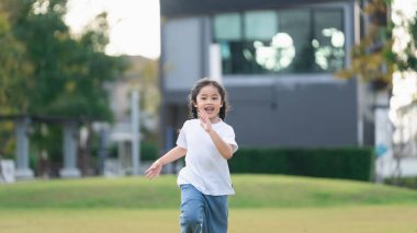 Neşeli çocuk güneşin altındaki bir parkta özgürce koşuyor, dışarıda oyun ve doğanın tadını çıkarıyor, mutluluğu ve çocukluk masumiyetini yakalıyor.