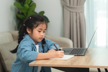 Evde dizüstü bilgisayar ve defterle okuyan genç bir kız, öğrenmeye ve not almaya odaklanmış, kapalı çalışma alanı, doğal ışıklandırma ve yeşillik