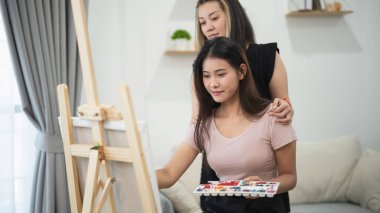 Sanatsal hobilerden hoşlanan genç kadınlar kapalı alanlarda birlikte, biri yaratıcı ifade ve rahatlama için resim tekniklerinde diğerine rehberlik ediyor.