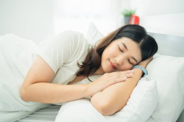 Huzurlu genç bir kadın, yumuşak yastıklar ve parlak doğal ışıklarla çevrili, rahat ve rahat bir şekilde evinde uyuyor..