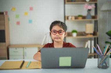 Modern Dekor ve Renkli Kırtasiyeyle çevrili Konforlu Çalışma Alanında Dizüstü bilgisayara Odaklanan Gözlüklü Genç Kız