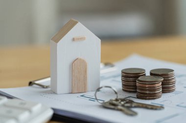 Yatırım, tasarruf ve gayrimenkul kavramlarını temsil eden yığınla madeni para ve anahtarla mali belgelere dayalı küçük ahşap ev modeli