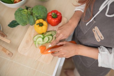 Fresh vegetable preparation in a cozy kitchen, focused hands slicing colorful ingredients on a wooden cutting board surrounded by healthy produce
