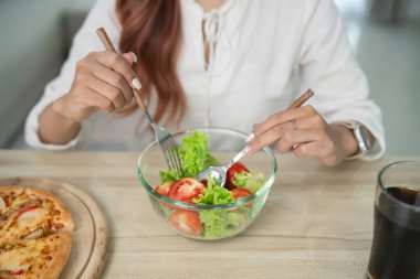 Modern yemek düzeninde çatal ve kaşıkla taze ve sağlıklı salata hazırlama Pizza ve meşrubat ile çevrili