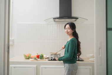 Genç bir kadın modern mutfakta sağlıklı yemekler pişiriyor, sebze hazırlıyor ve taze malzemelerle aşçılık deneyiminden zevk alıyor, ev yemeği kavramından.