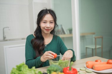 Genç kadın, modern mutfakta sebzelerle taze salata, sağlıklı beslenme tarzı ve refah ve refah için beslenme konsepti hazırlıyor.
