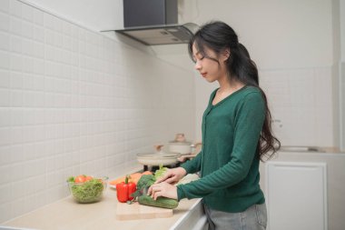 Genç bir kadın modern mutfakta yemek pişiriyor, sağlıklı malzemelerle çevrili taze sebzeleri doğruyor, odaklanmış ve özenle yemek hazırlıyor.
