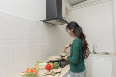 Genç bir kadın modern mutfakta sebze pişiriyor, taze malzemelerle sağlıklı yemekler hazırlıyor ve evde tek başına yemek pişirme deneyiminin tadını çıkarıyor.