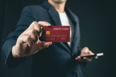 Person in Suit Holding Credit Card with Smartphone in Other Hand on Dark Background Showcasing Modern Payment and Financial Transactions Concept
